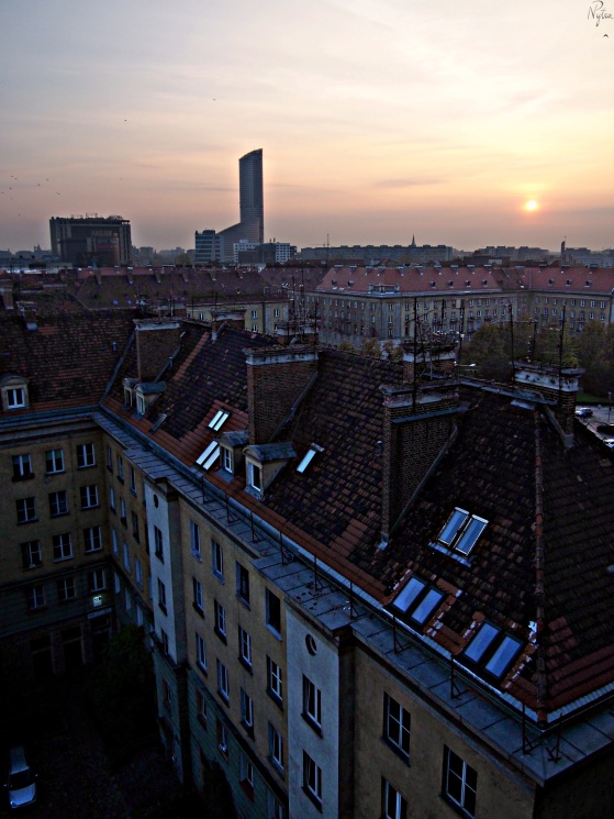 Zachód słońca nad dachami kamienic. Po lewej Arkady Wrocławskie i Sky Tower.